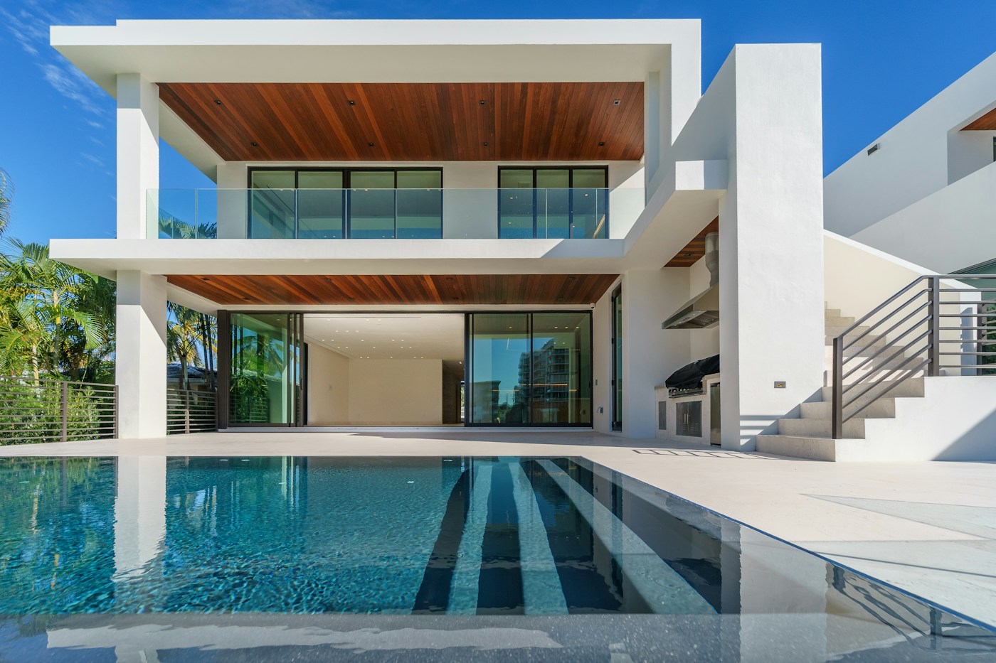 A white modern home with timber ceilings opening onto a blue swimming pool